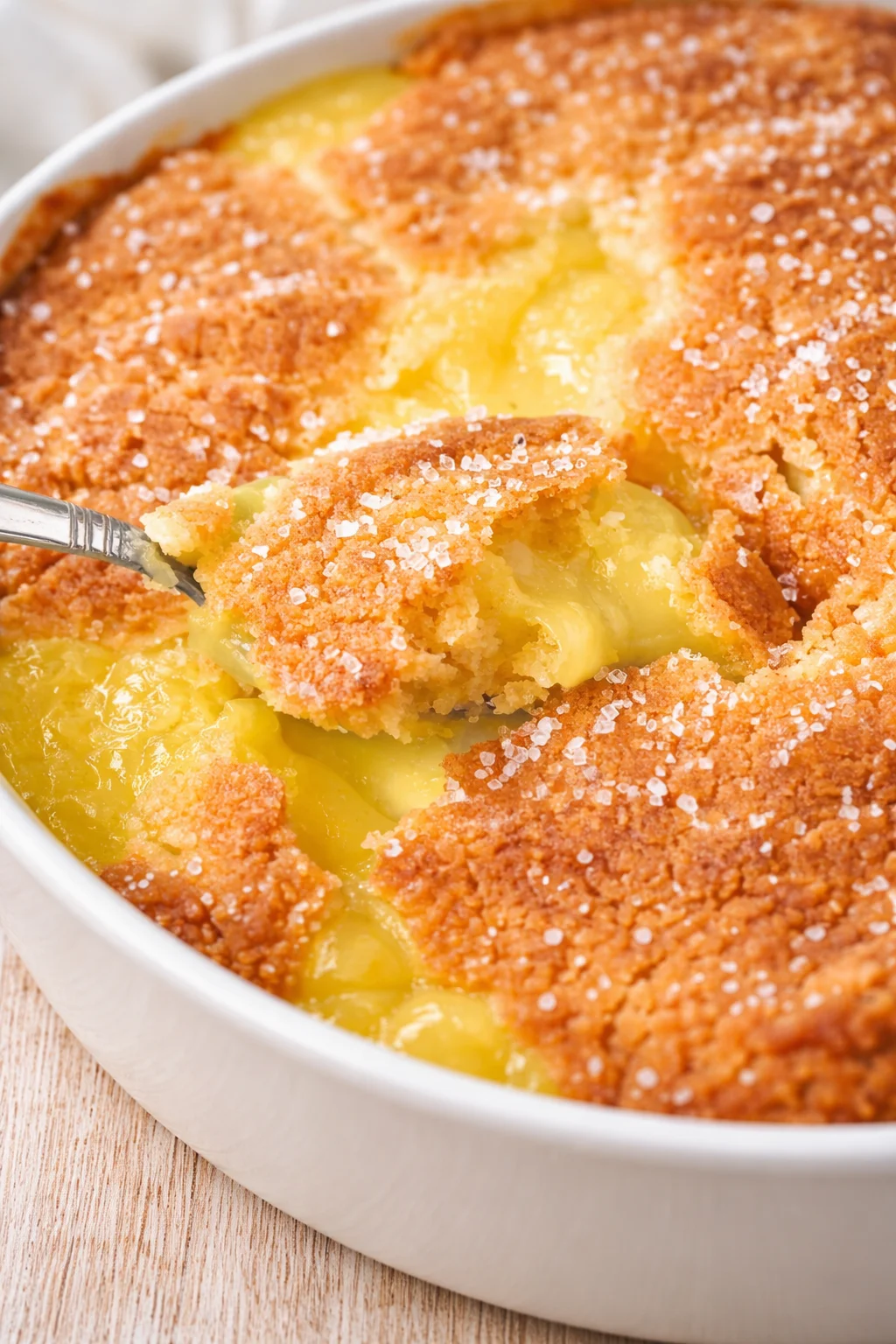 Close-up of lemon-curd crumble in a white baking dish with a spoon scooping gooey filling.