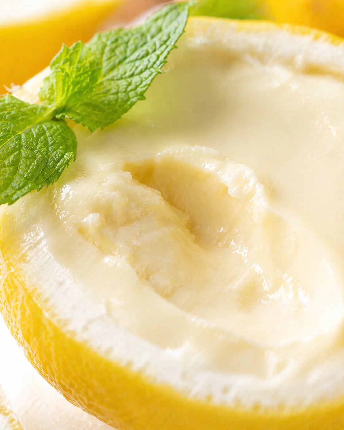 Close-up of a halved lemon with a mint leaf on its rind and pale creamy interior