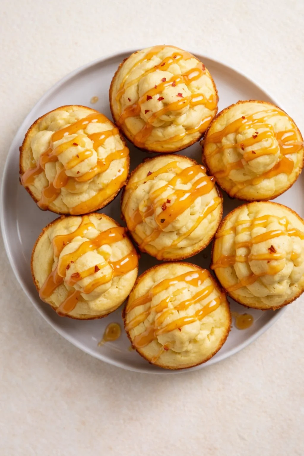 Nine mini lemon cupcakes on a white plate, topped with pale frosting and orange drizzle.