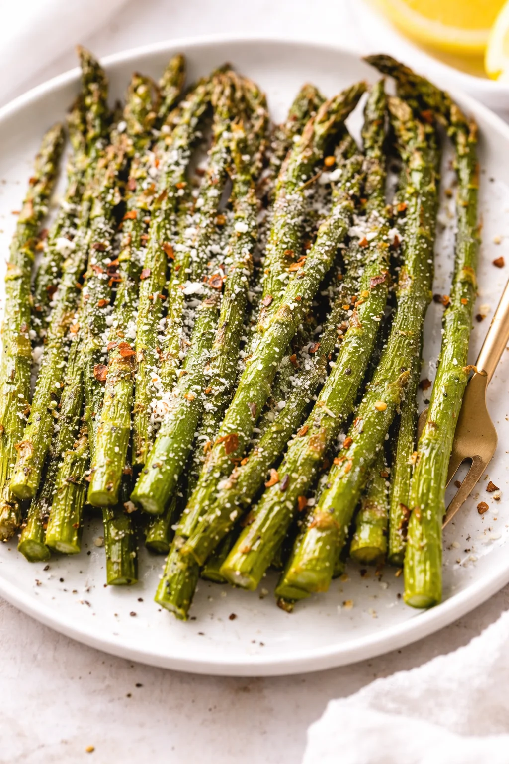 Bright green asparagus spears on a white plate, sprinkled with parmesan and red-pepper flakes; lemon wedge in background.
