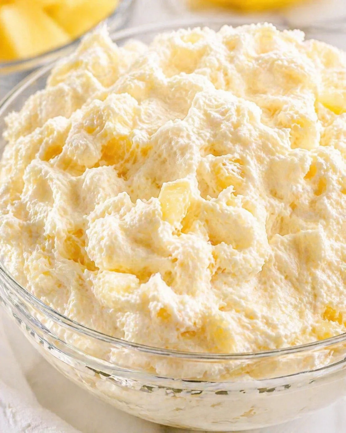 glass bowl of fluffy whipped-cream with pineapple chunks in a bright kitchen setting