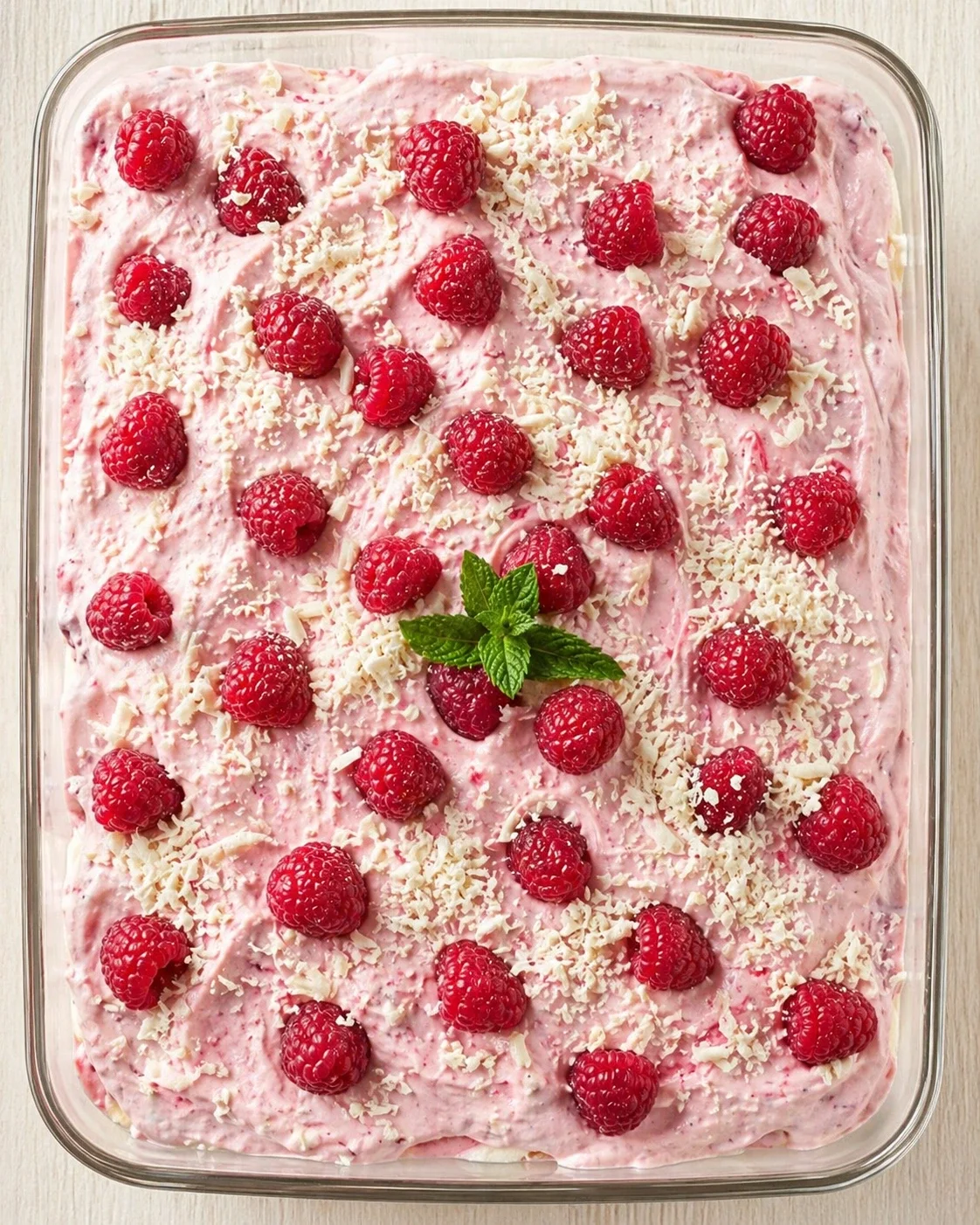 pink raspberry dessert in a glass dish topped with raspberries, white chocolate shavings, and mint