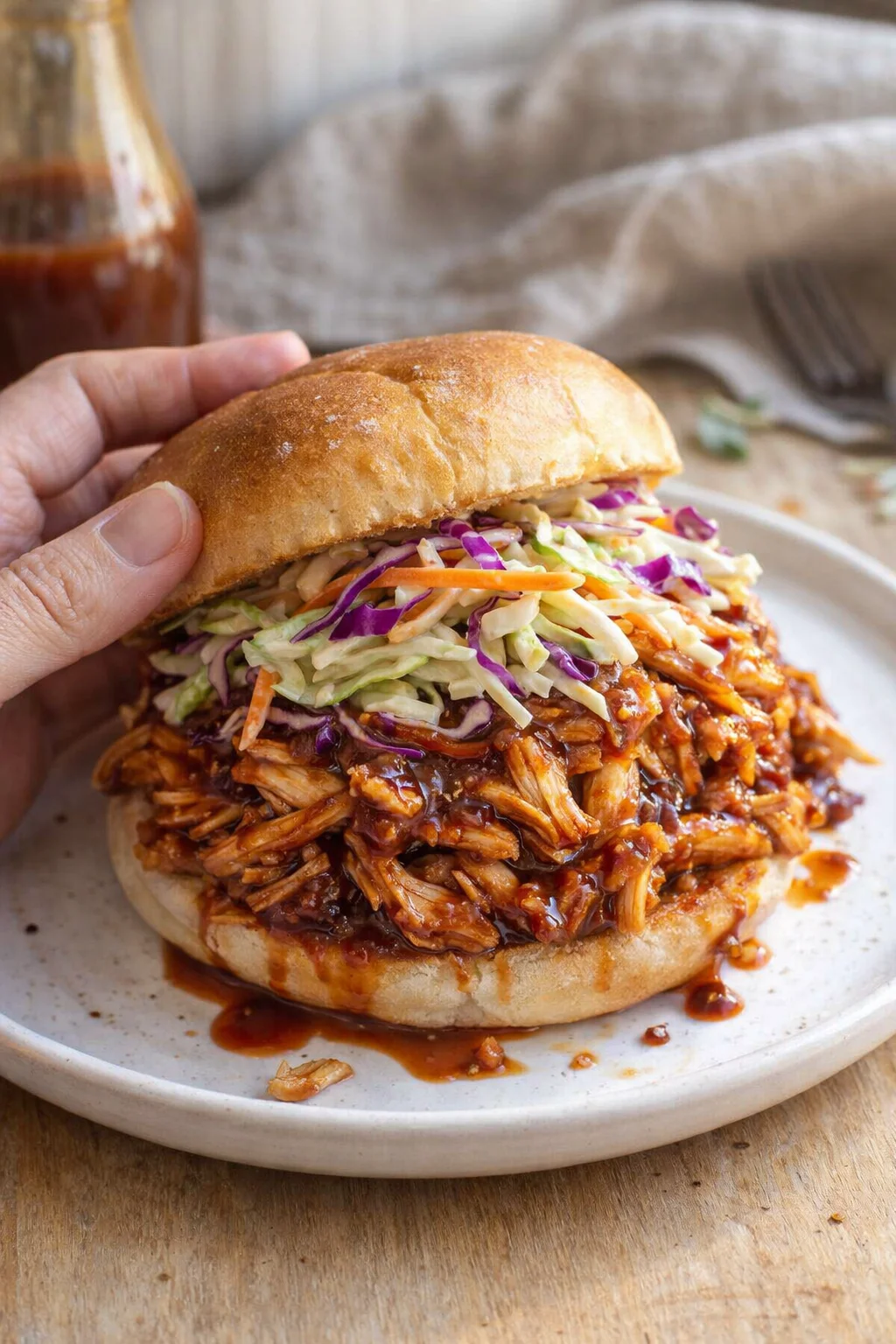 Close-up of a pulled pork sandwich with barbecue sauce and colorful slaw on a plate.
