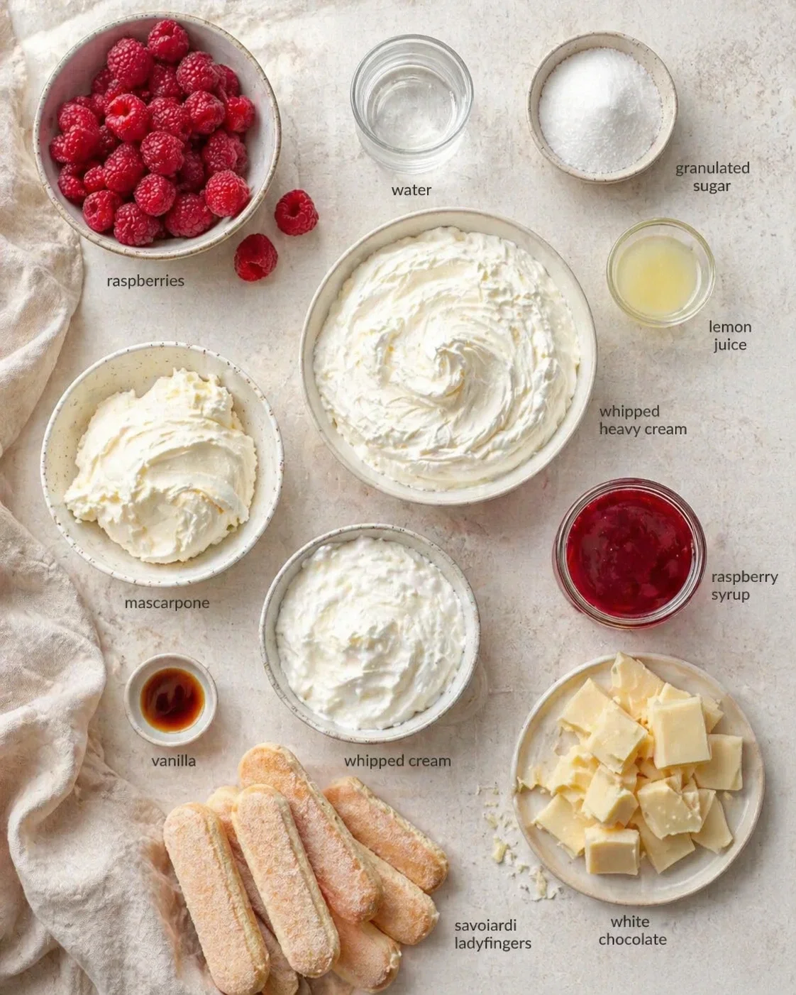 top-down view of raspberries, whipped cream, mascarpone, vanilla, sugar, and cookies arranged for a recipe