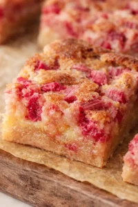 Close-up of rhubarb-streusel bars on parchment atop a wooden board.