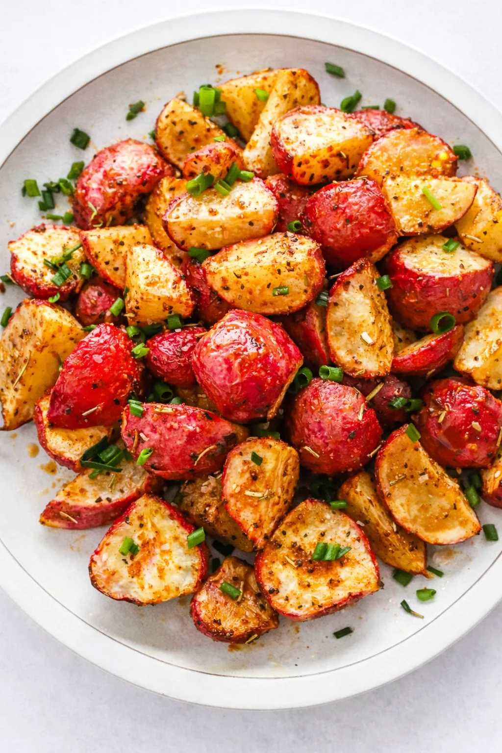 crispy roasted red and yellow potato wedges with chopped green onions on a white plate