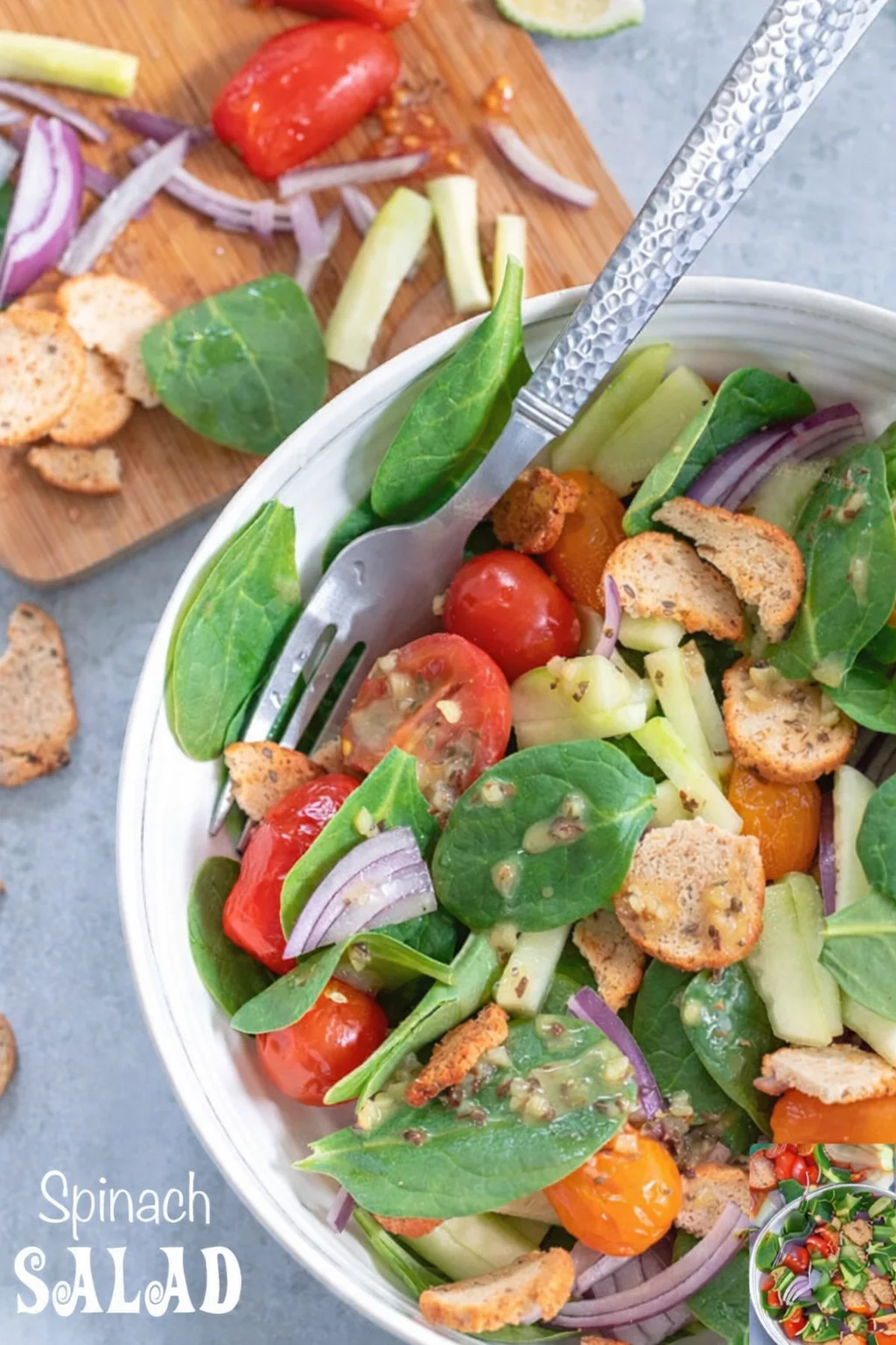Bright spinach salad with tomatoes, cucumber, red onion, and croutons in a white bowl