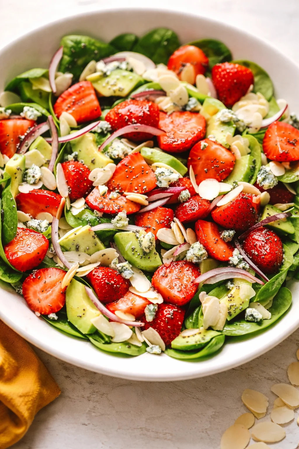 white bowl of fresh baby spinach salad with strawberries, avocado, red onion, almond slivers, and blue cheese