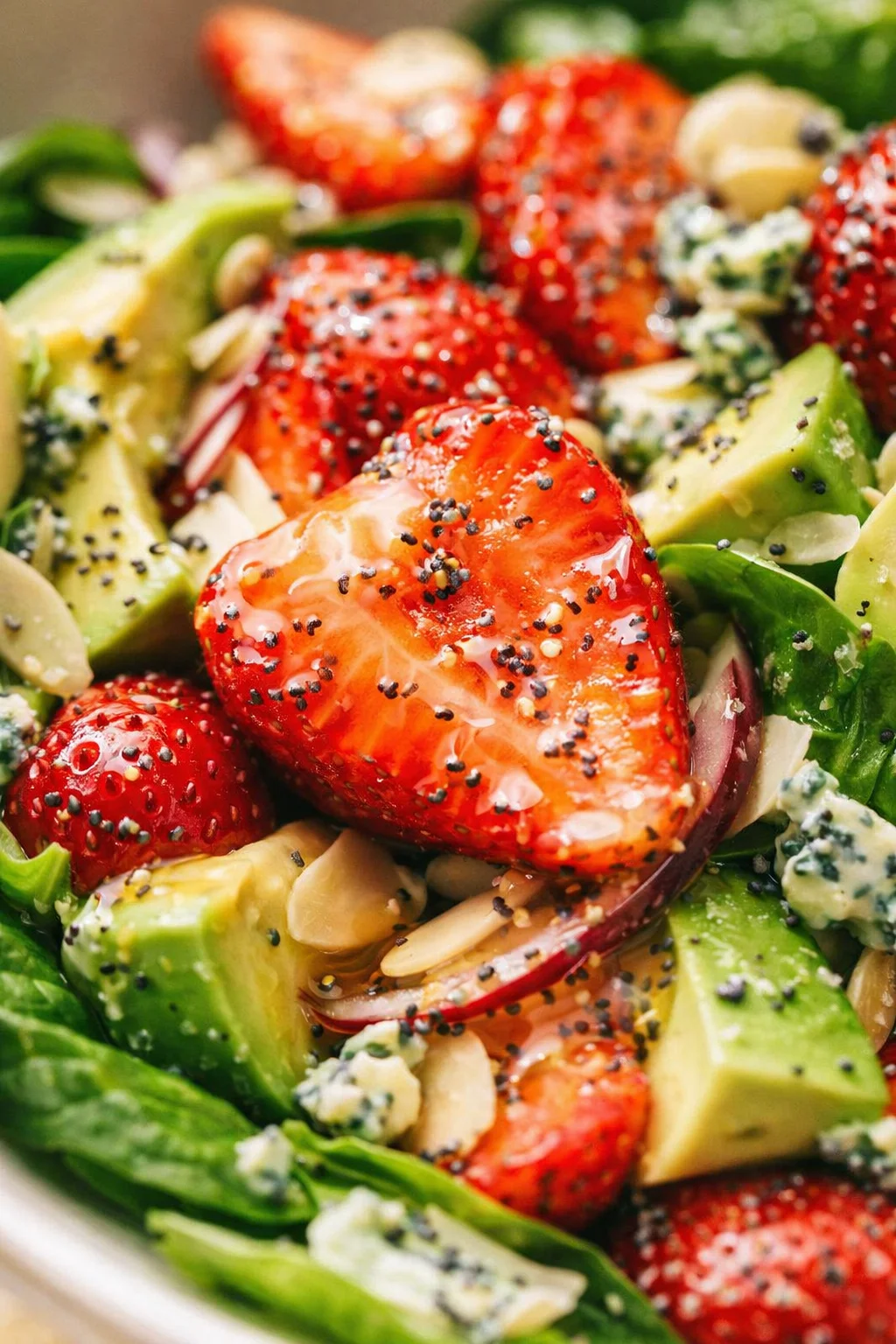 Close-up of strawberry-avocado salad with greens, red onion, almonds, and blue cheese.