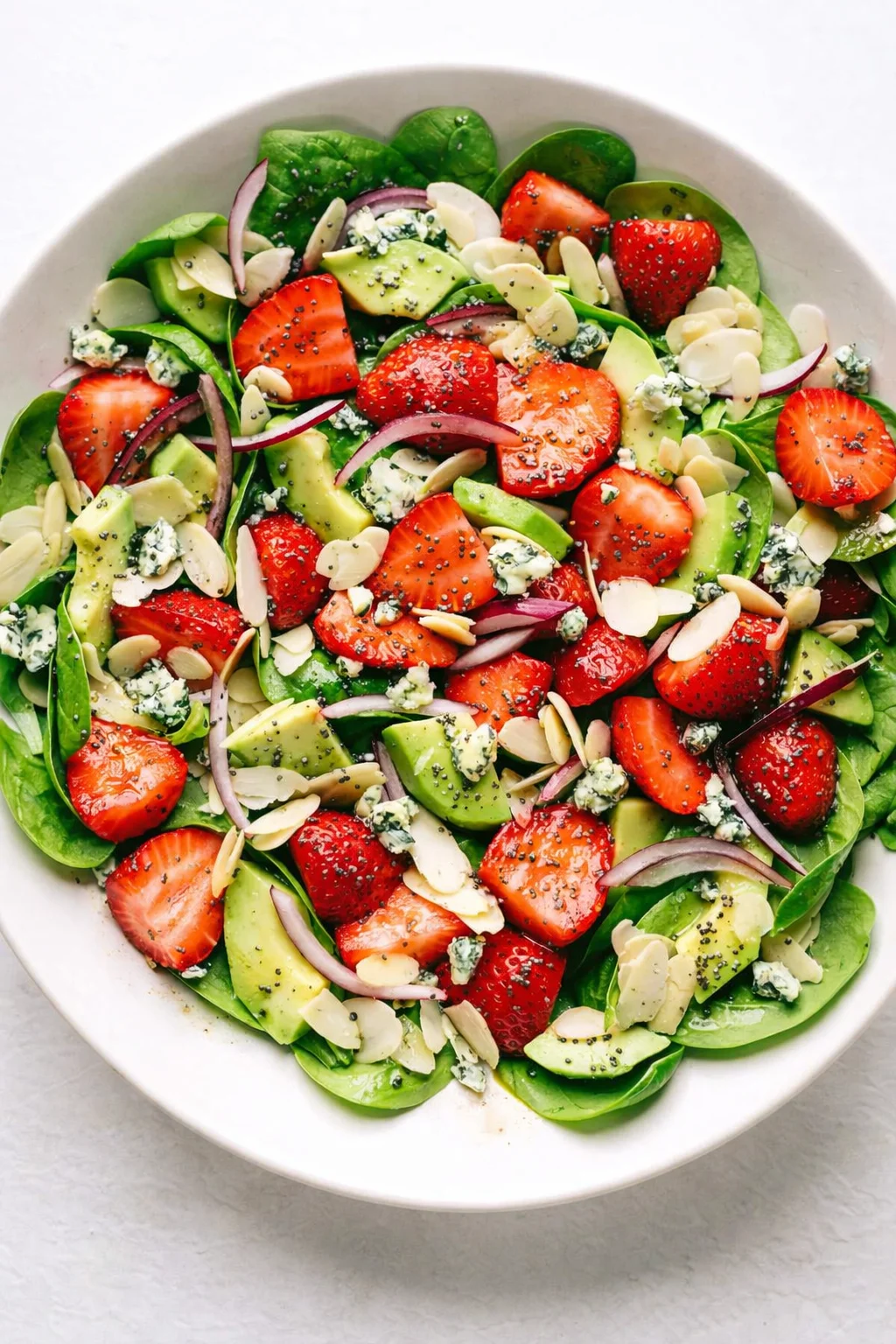 colorful strawberry avocado spinach salad with red onion, almonds, and blue cheese.