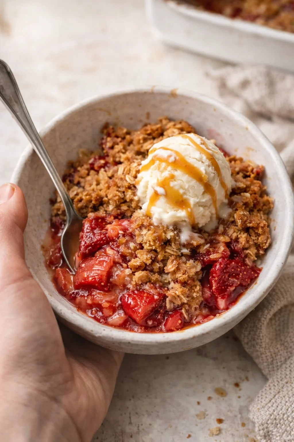 Vanilla ice cream atop strawberry crumble in a speckled ceramic bowl.