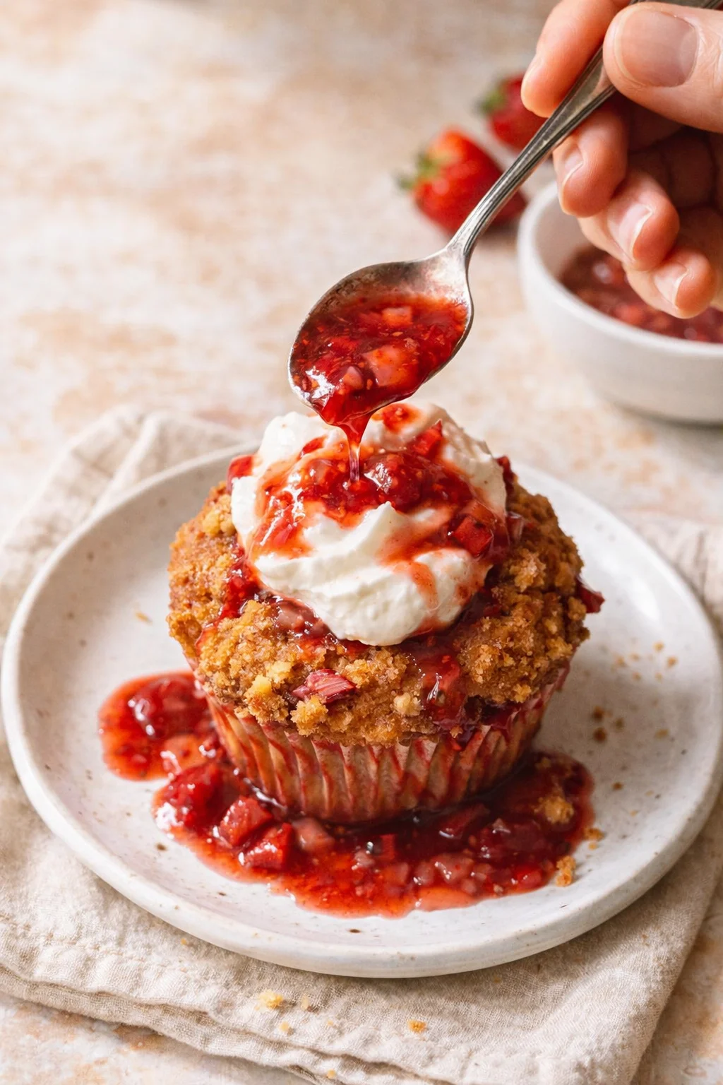Golden crumble muffin with whipped cream and strawberry sauce on a plate.