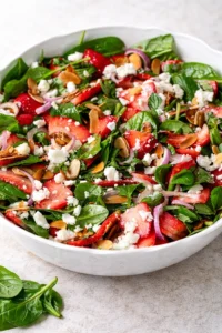 A white bowl filled with strawberry spinach salad topped with feta, red onion, and almond slices.