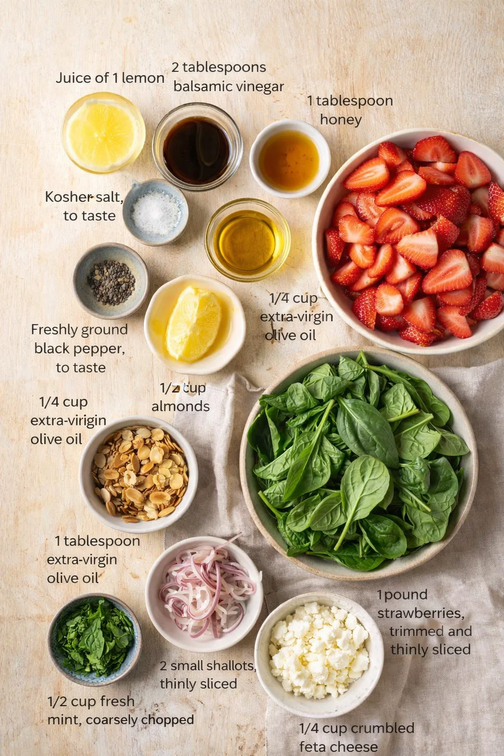 Overhead shot of strawberry spinach salad ingredients arranged on a wooden surface.