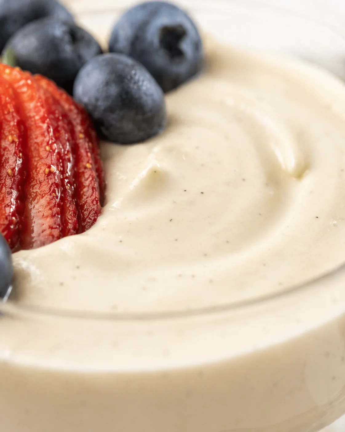 Close-up of creamy vanilla yogurt with blueberries and a sliced strawberry