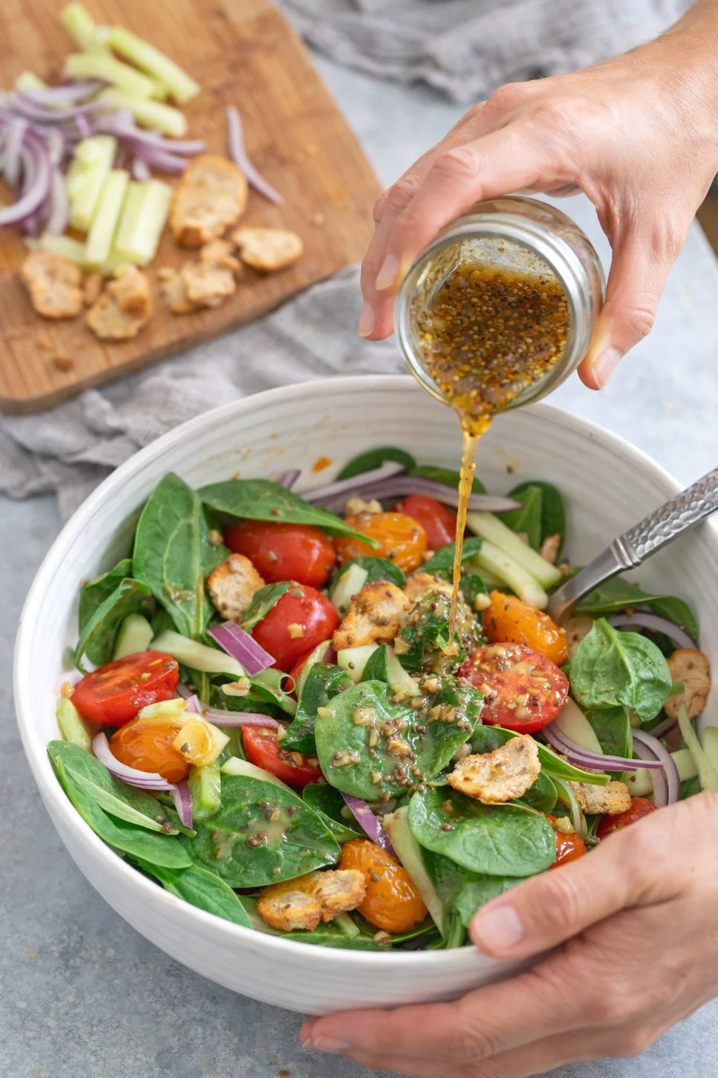 Fresh spinach salad topped with cherry tomatoes, cucumbers, onions, and bagel chips