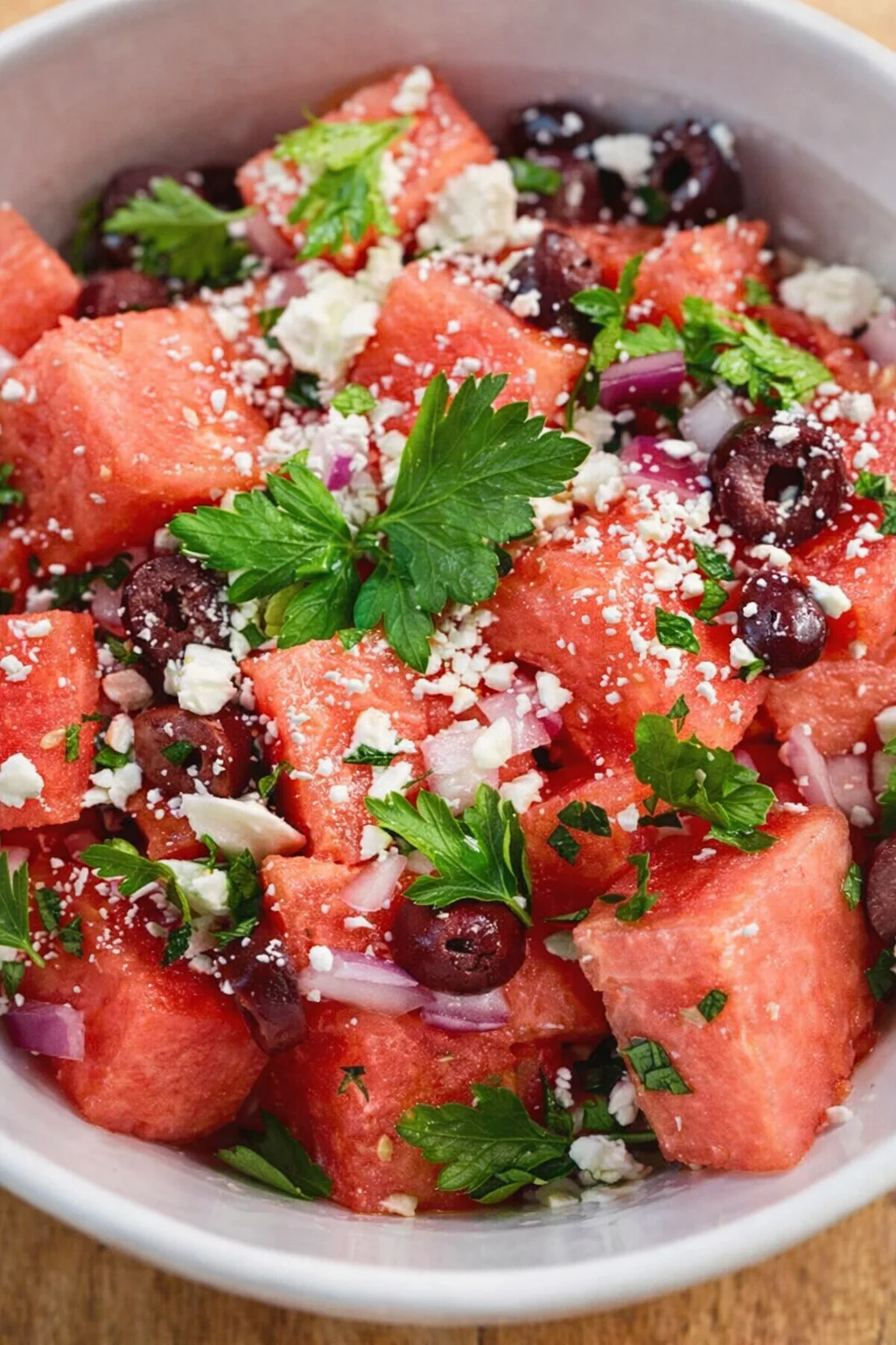 white ceramic bowl with watermelon cubes, olives, red onion, feta, and parsley