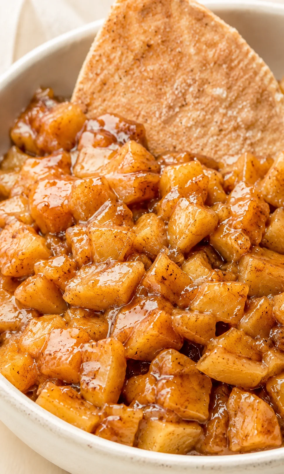close-up of caramel-glazed, diced apples in a pan with a crispy tortilla chip