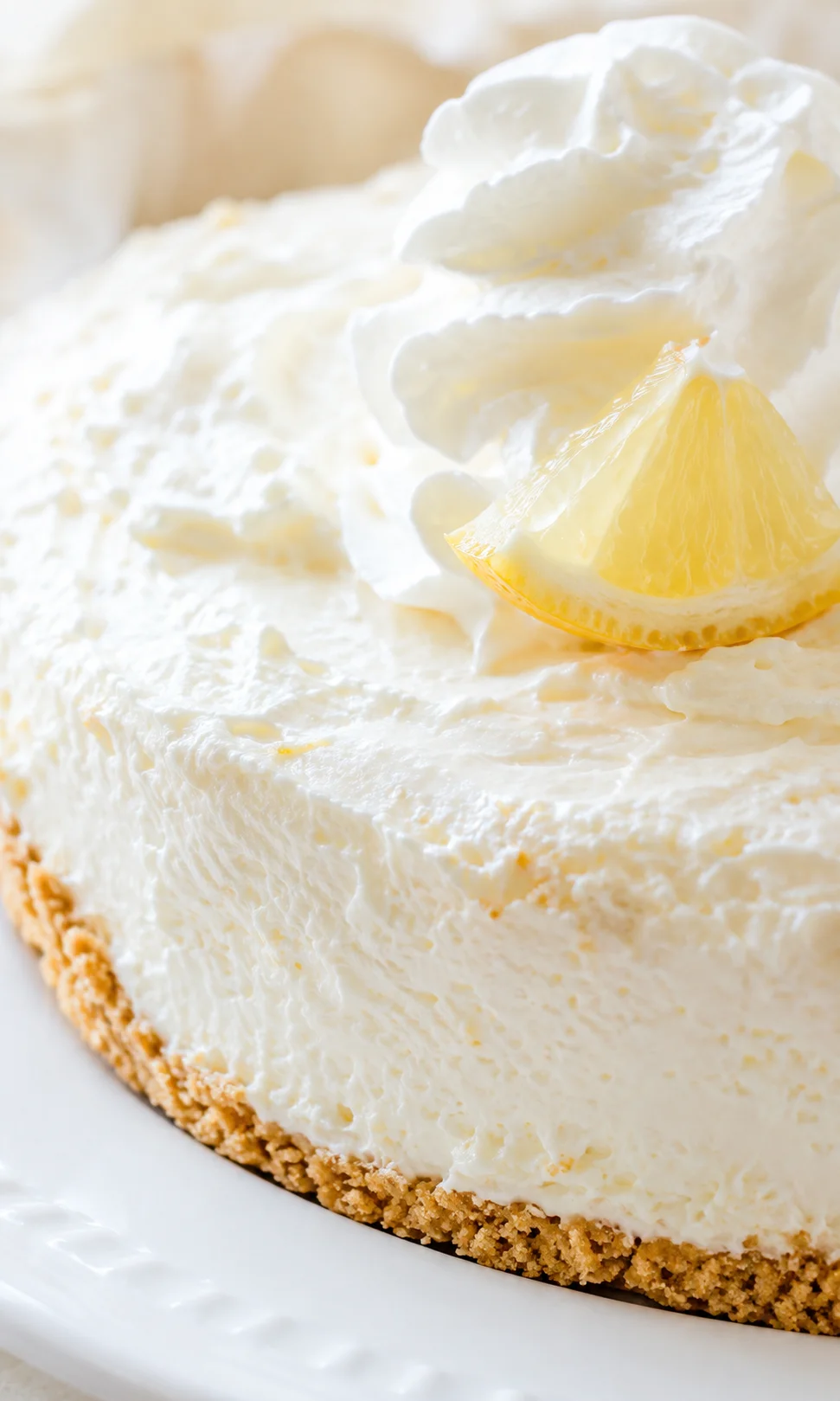 Close-up of lemon cheesecake with whipped cream and lemon wedge garnish.