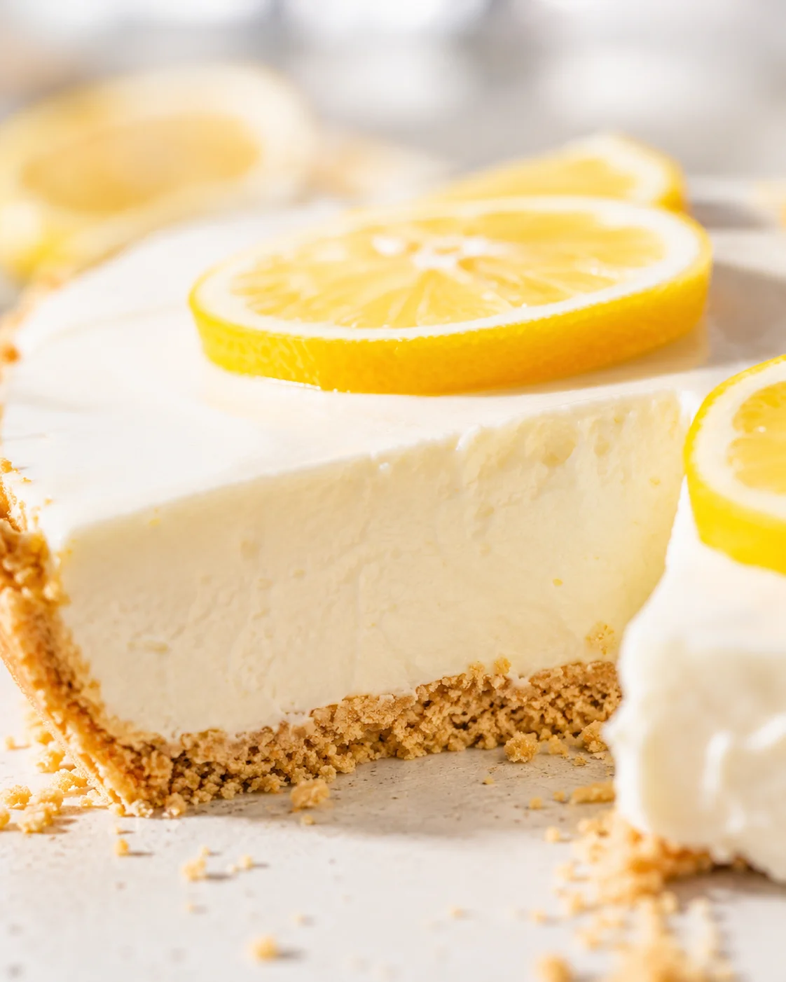 Close-up shot of a creamy lemon cheesecake with a crumb crust and bright lemon slices on top.