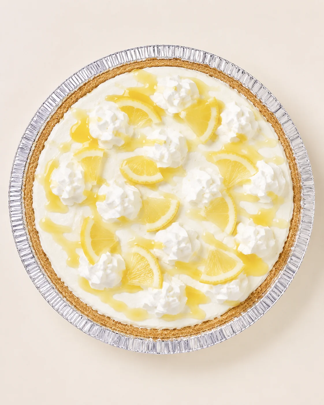 top-view lemon cheesecake pie topped with whipped cream and lemon slices in a foil pan