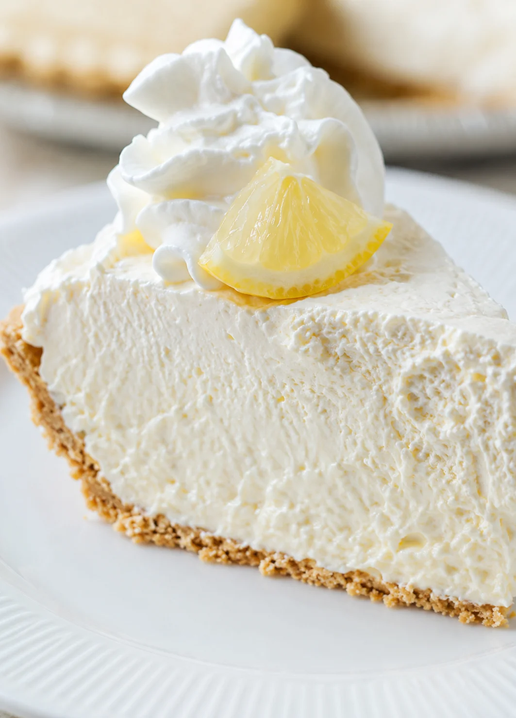 Creamy lemon cheesecake slice on a white plate topped with whipped cream and a lemon wedge.