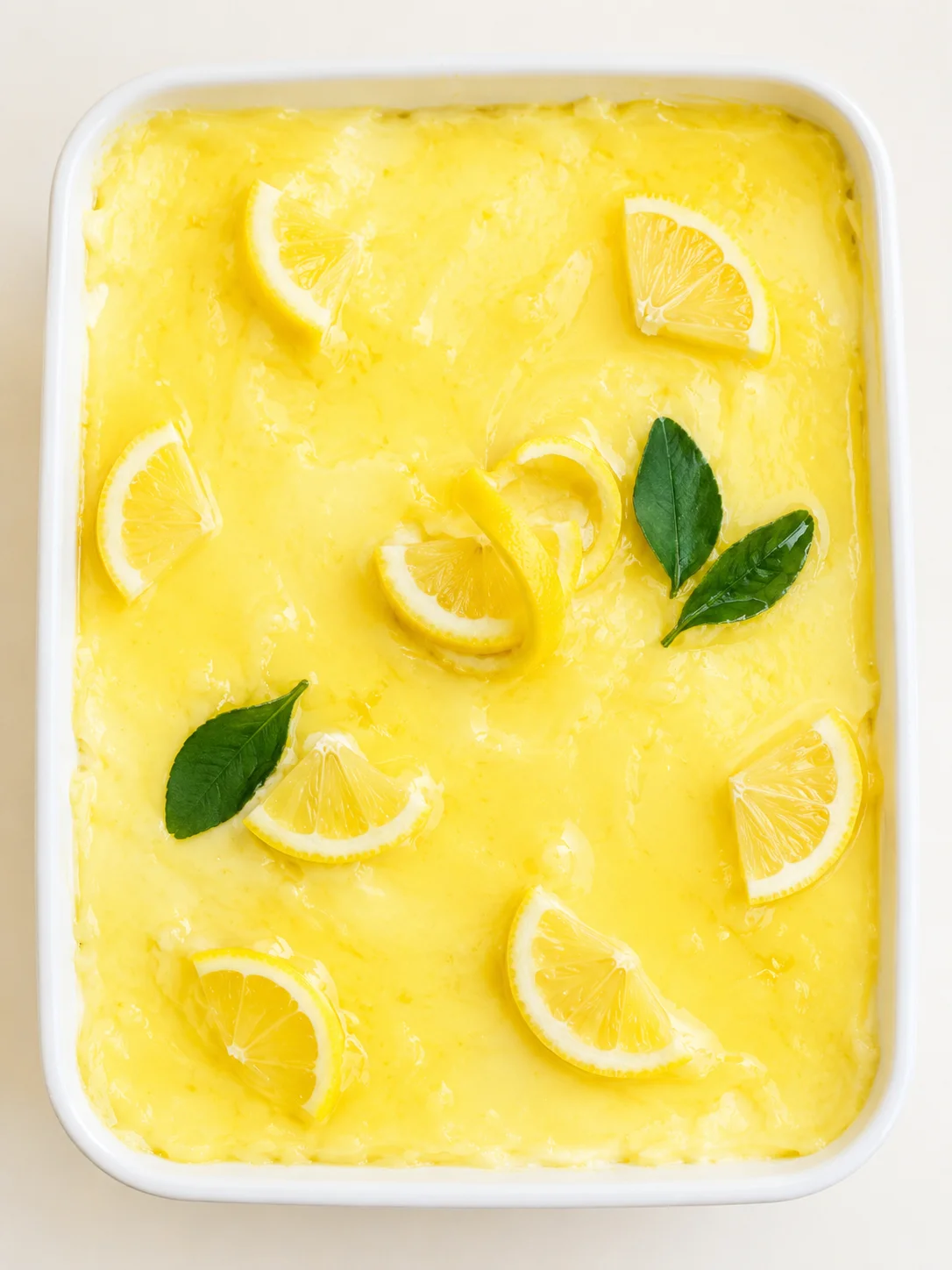 white rectangular dish filled with lemon-curd topped with lemon wedges and green leaves