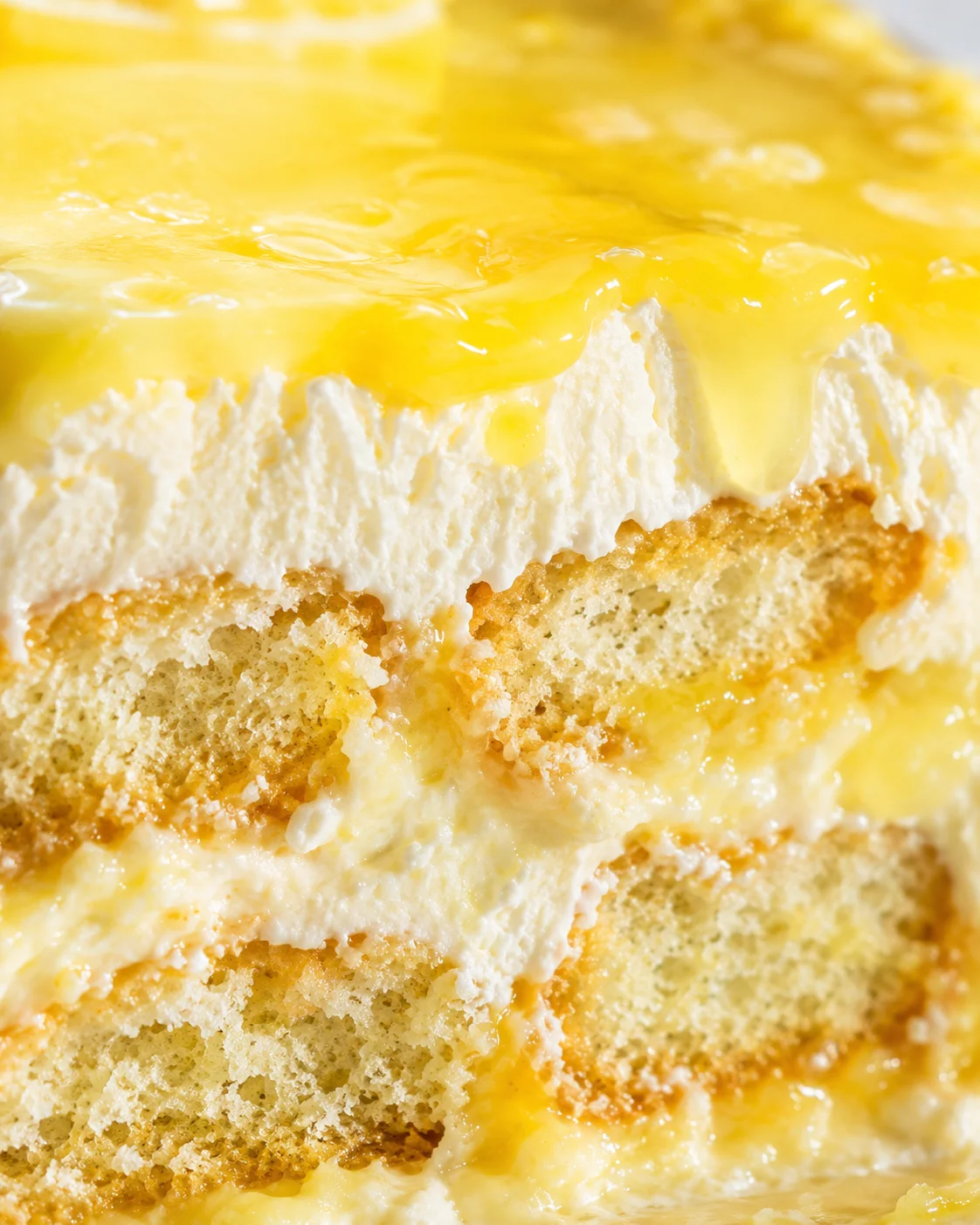 Close-up of a layered lemon cake with white cream and glossy lemon glaze.