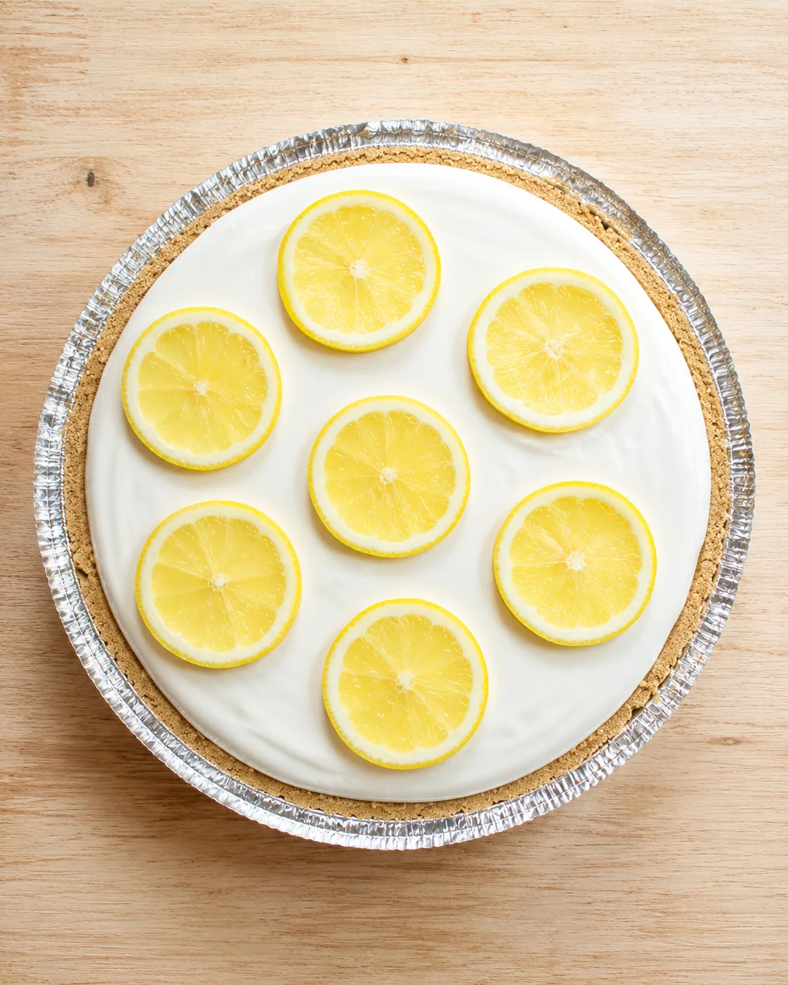 Top-down view of lemon-slice cheesecake in a foil pan on a wooden table
