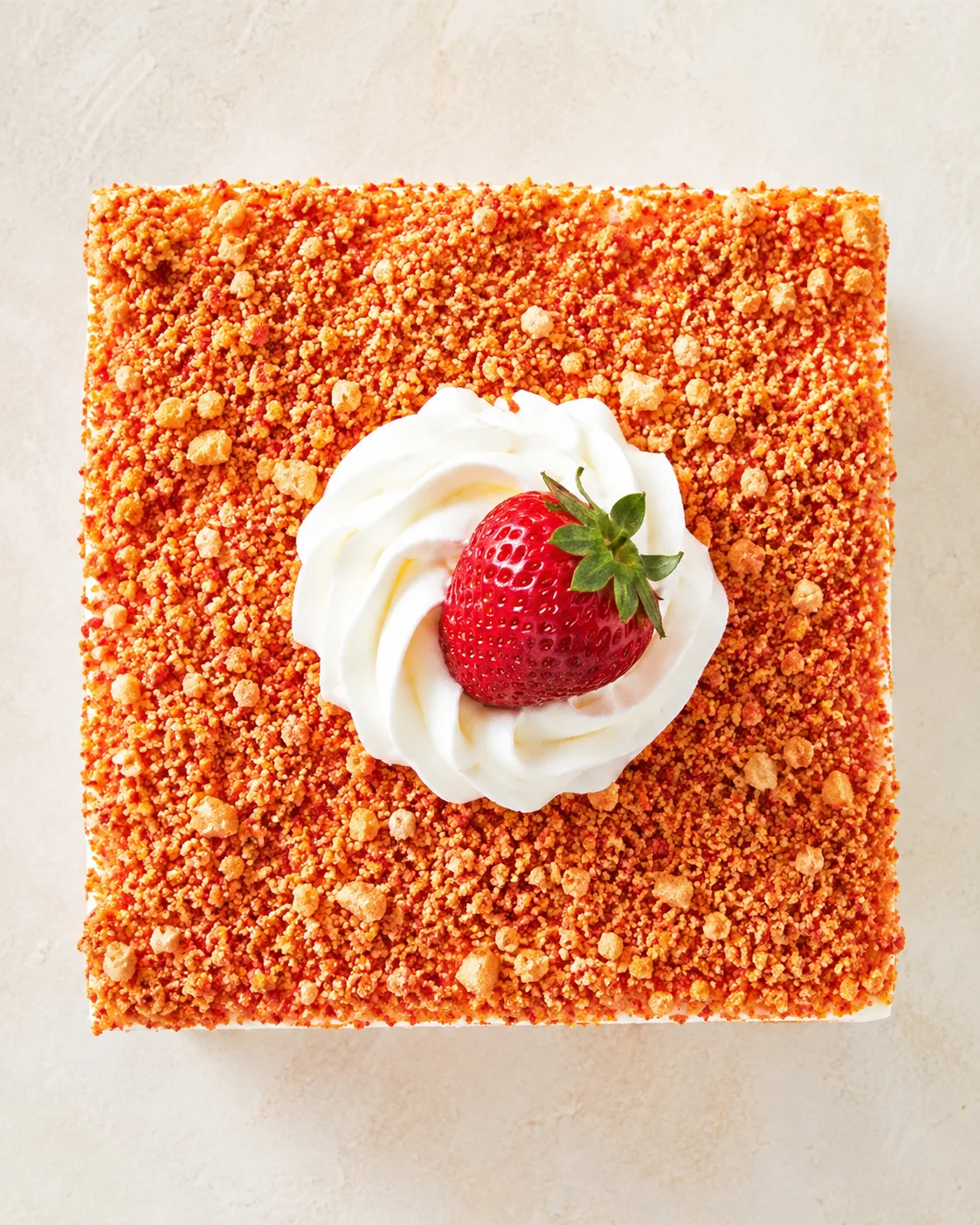 top-down view of square orange crumble cake with whipped cream rosette and strawberry