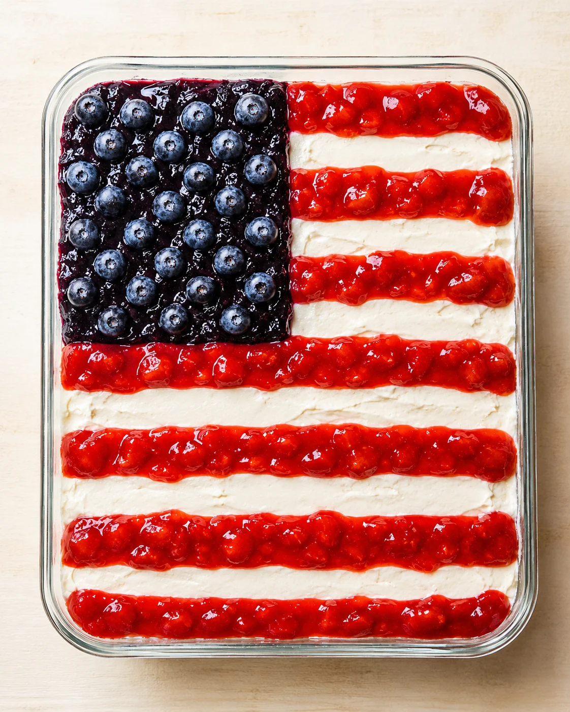 Overhead shot of a glass dish with a white-frosted cake decorated as a flag using blueberries and red jam.