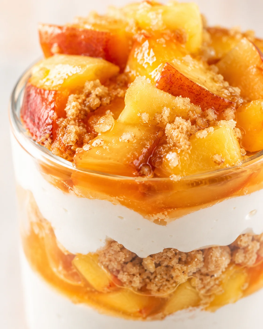Layered peach parfait in a clear glass with crumble and caramel sauce.