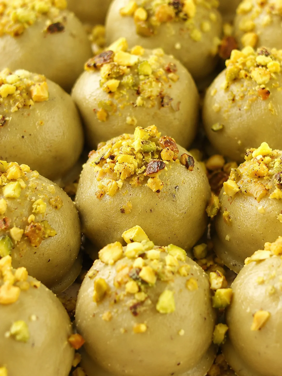 Close-up of greenish-gray pistachio-truffle bites topped with chopped pistachios, filling the frame