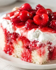 Close-up of a vanilla sponge cake slice topped with glossy red cherries and whipped cream.