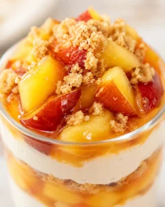 Close-up of peach cheesecake parfait top, glossy diced peaches, brown sugar crumble, creamy filling.