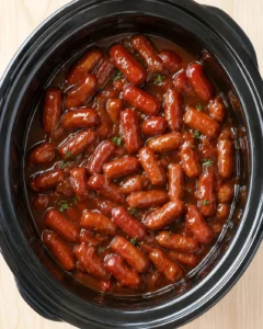 overhead view of glossy glazed sausages in a black slow cooker, garnished with parsley