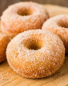 Close-up of freshly baked pumpkin donuts coated in cinnamon sugar and arranged on a wooden surface