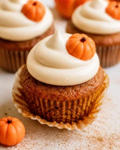 Close-up of a pumpkin cupcake topped with cream cheese frosting and a tiny pumpkin decoration.