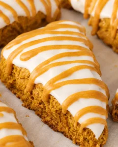 Close-up of freshly baked pumpkin scone drizzled with white glaze and caramel sauce.