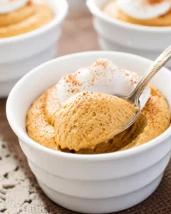 Creamy pumpkin mousse topped with whipped cream in a white bowl.
