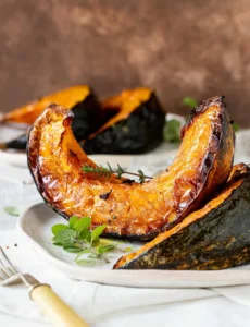 Brown background, white surface, plates containing blistered pumpkin wedges, fresh herbs