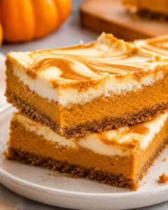 Delicious pumpkin cheesecake bars with marbled swirl topping on a white plate.