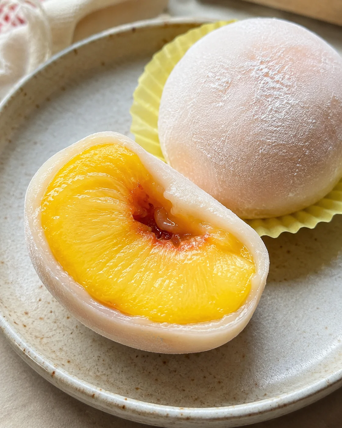 Close-up of a soft, round peach mochi with a sliced peach revealing its juicy interior.