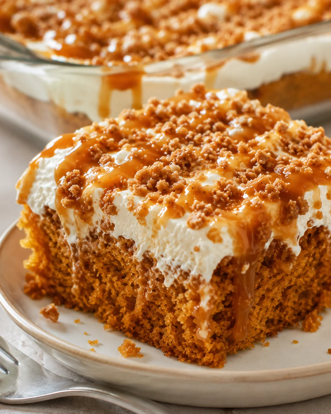 Delicious slice of moist pumpkin cake topped with whipped cream, caramel, and crumble