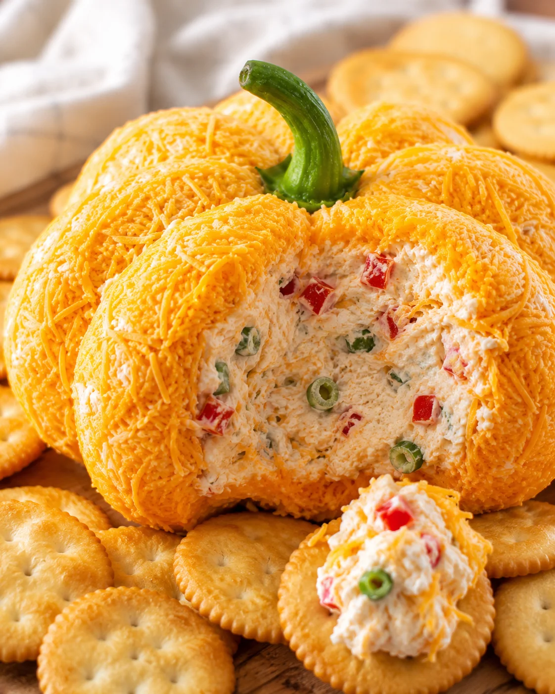 Decorative pumpkin-shaped cheeseball with shredded cheese and vegetables on crackers
