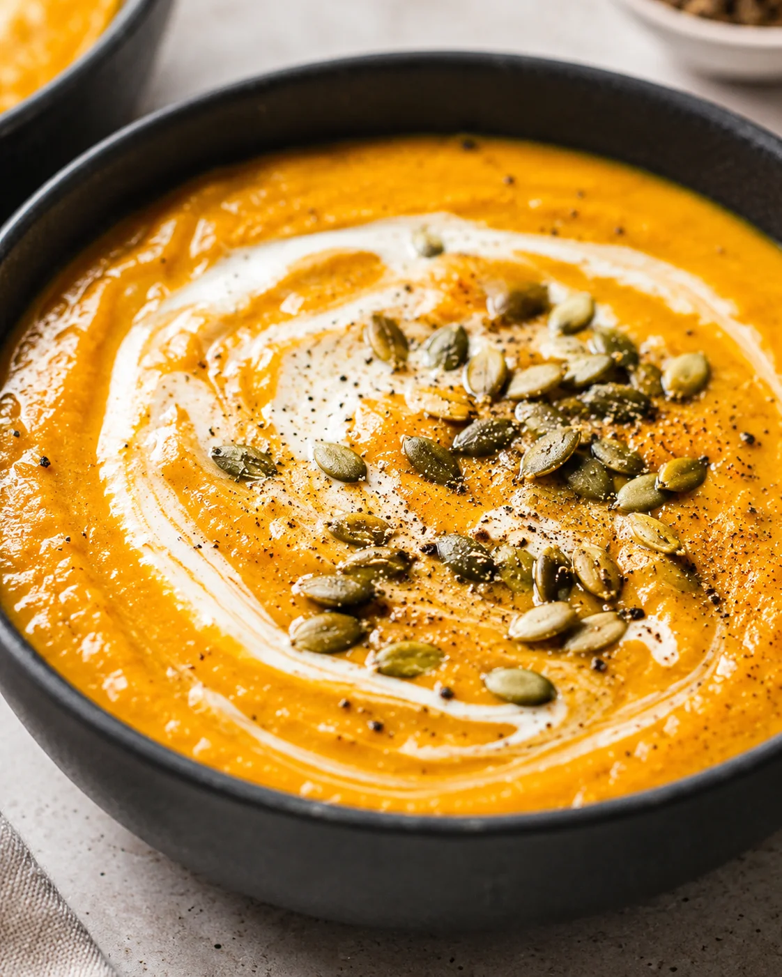 A bowl of creamy pumpkin soup garnished with toasted pepitas and a swirl of cream