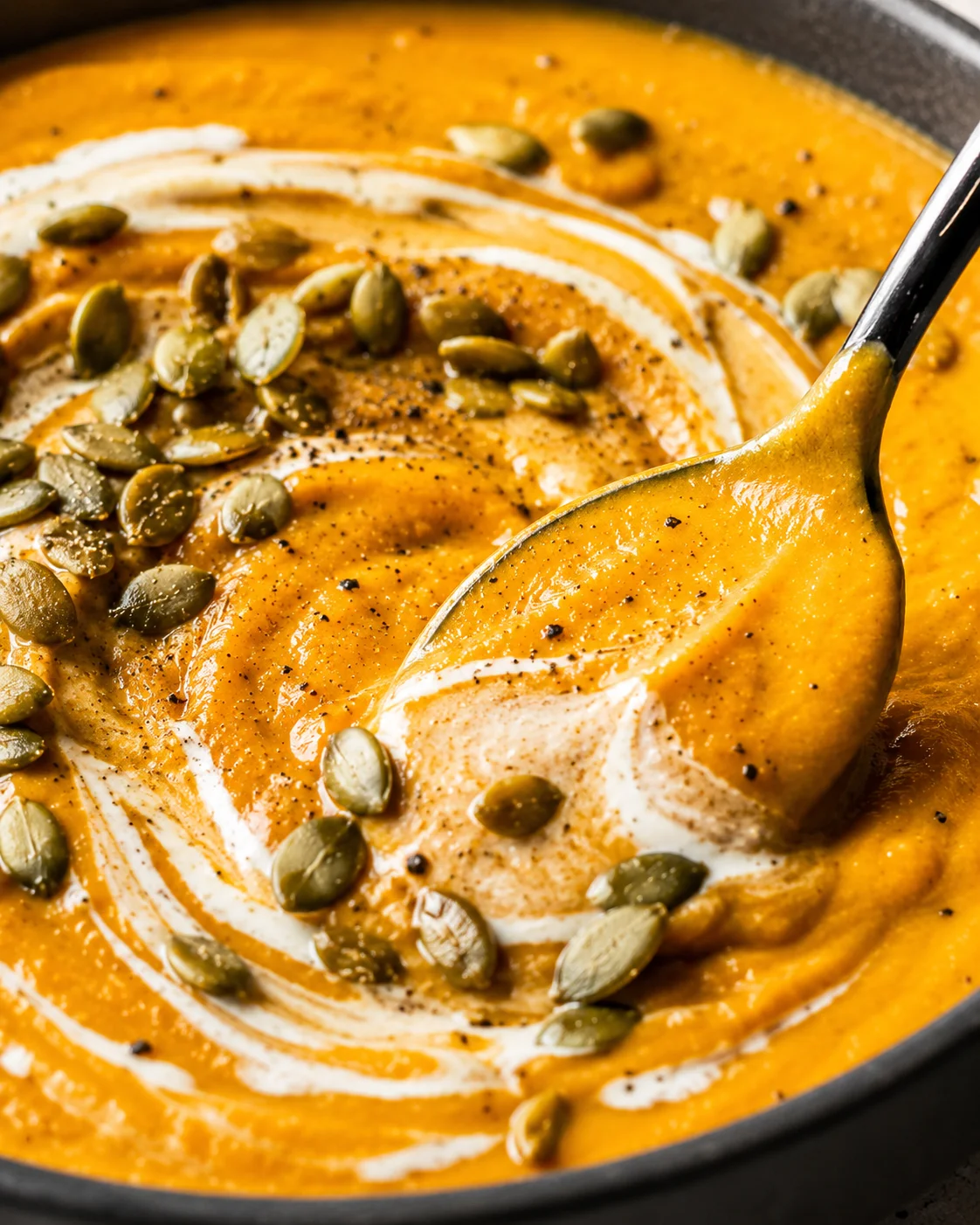 Close-up of creamy pumpkin soup garnished with toasted pepitas and a swirl of cream