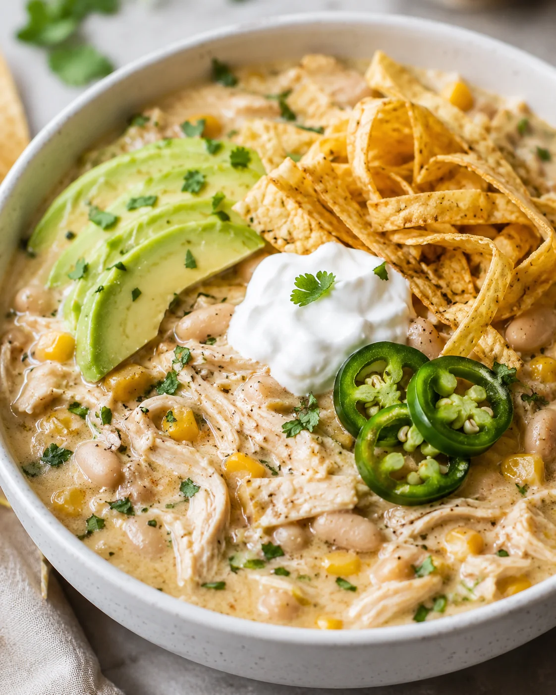 A bowl of creamy white chicken chili topped with avocado, jalapeños, and sour cream.