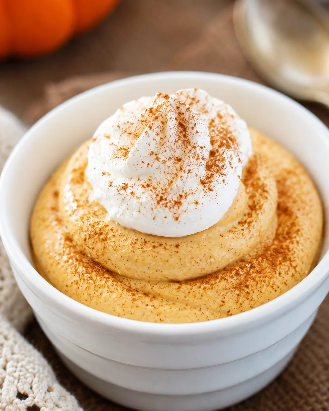 Creamy pumpkin mousse topped with whipped cream and cinnamon in a white bowl