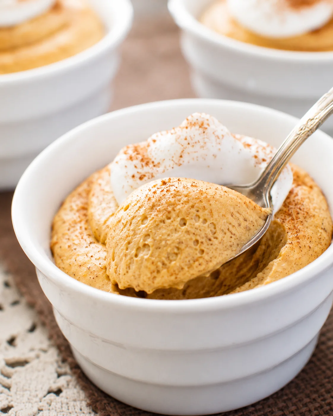 Creamy pumpkin mousse topped with whipped cream in a white bowl.